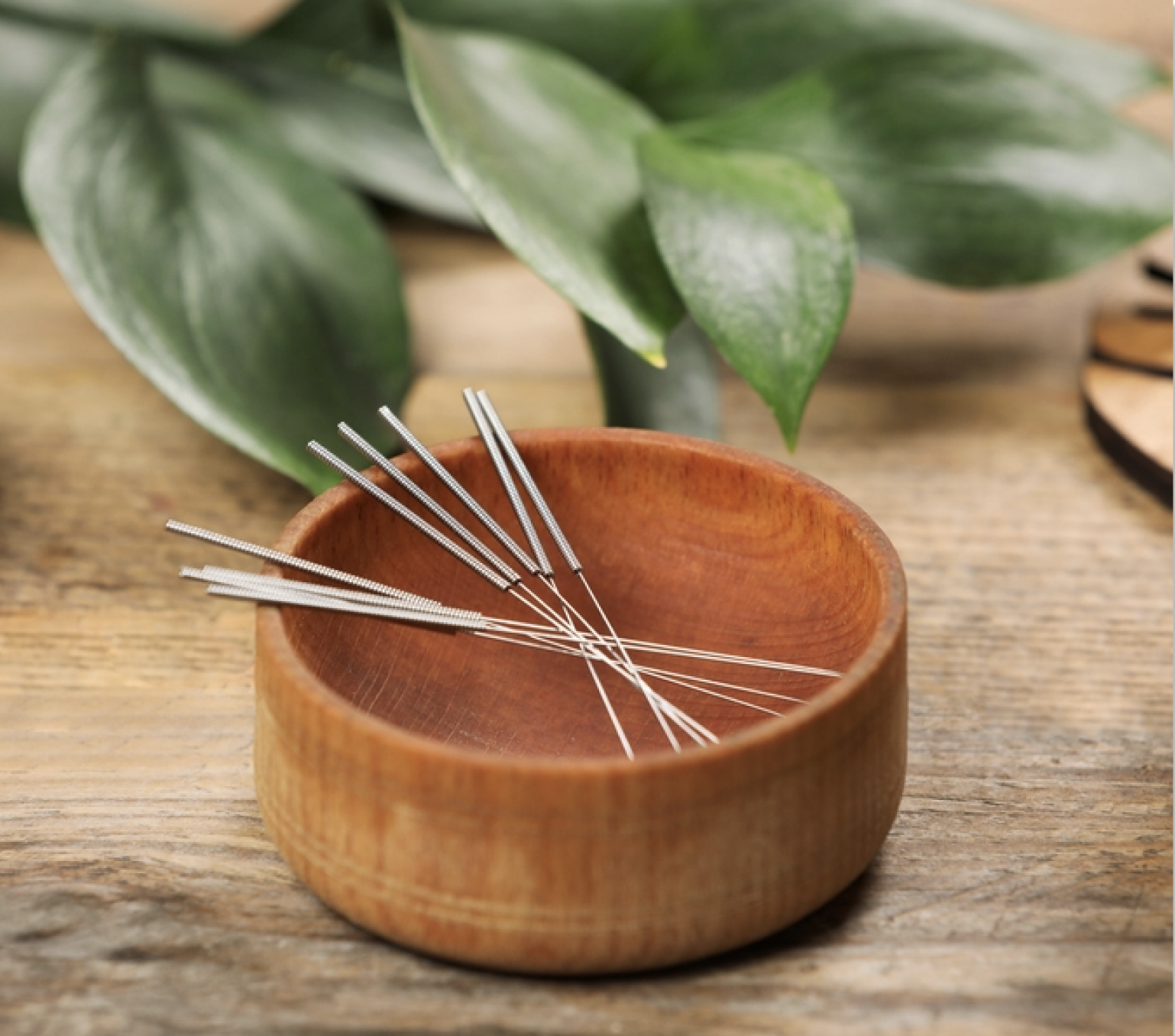 Acupuncture needles displayed in a bowl made of wood, resting on a wooden tabletop.